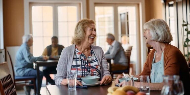 Elderly Friends Sharing Conversation in Dining Room at Assisted Living Community