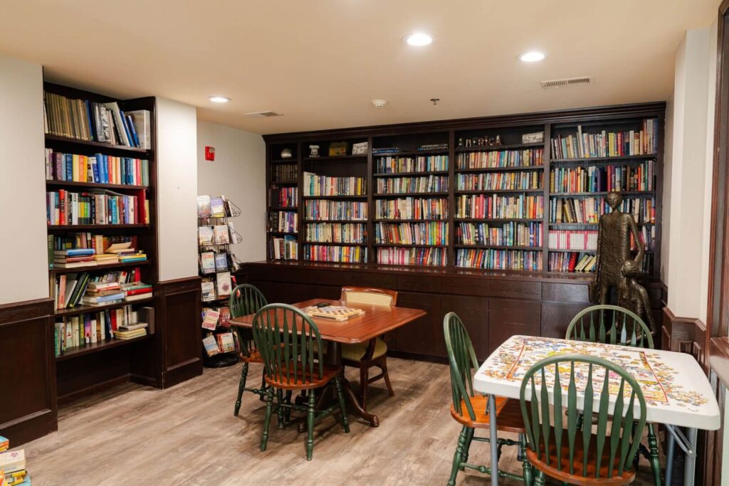Cozy Library With Floor-To-Ceiling Bookshelves And Puzzle Tables At Assisted Living Facility