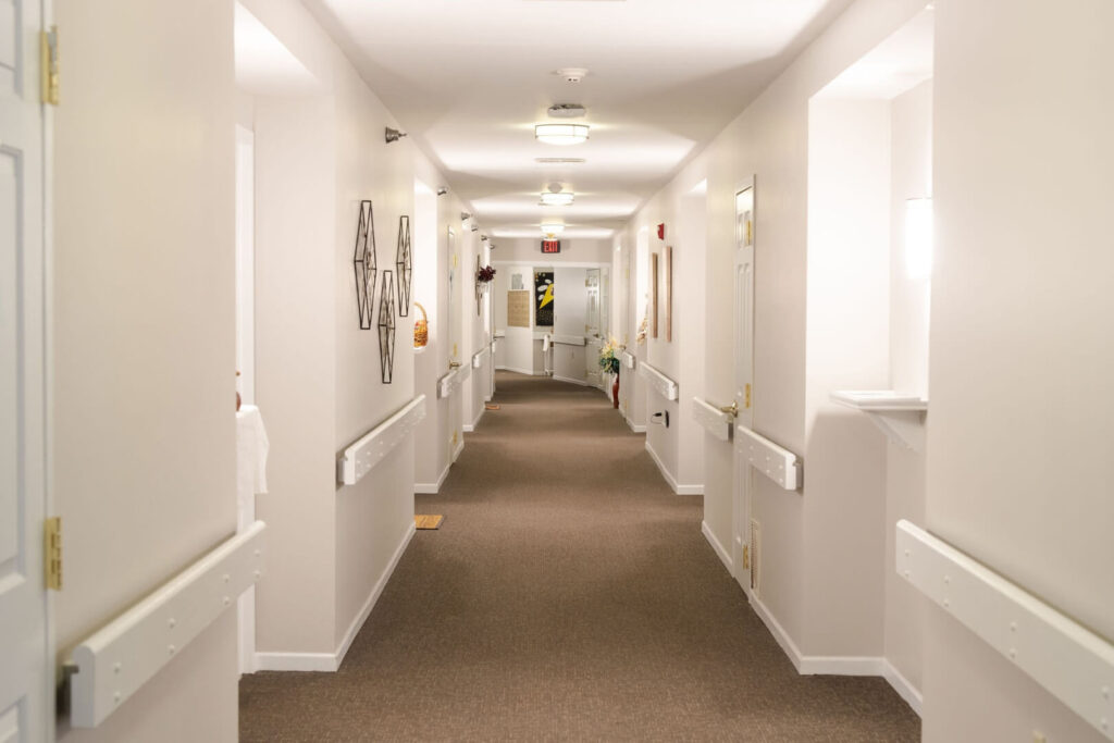 Wide Carpeted Hallway With Handrails Leading To Resident Rooms At Assisted Living Facility