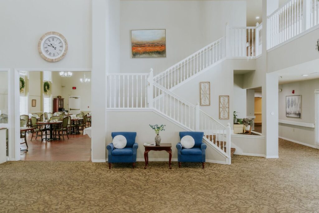 Bright Grand Lobby With Sweeping Staircase And Sitting Area At Assisted Living Facility
