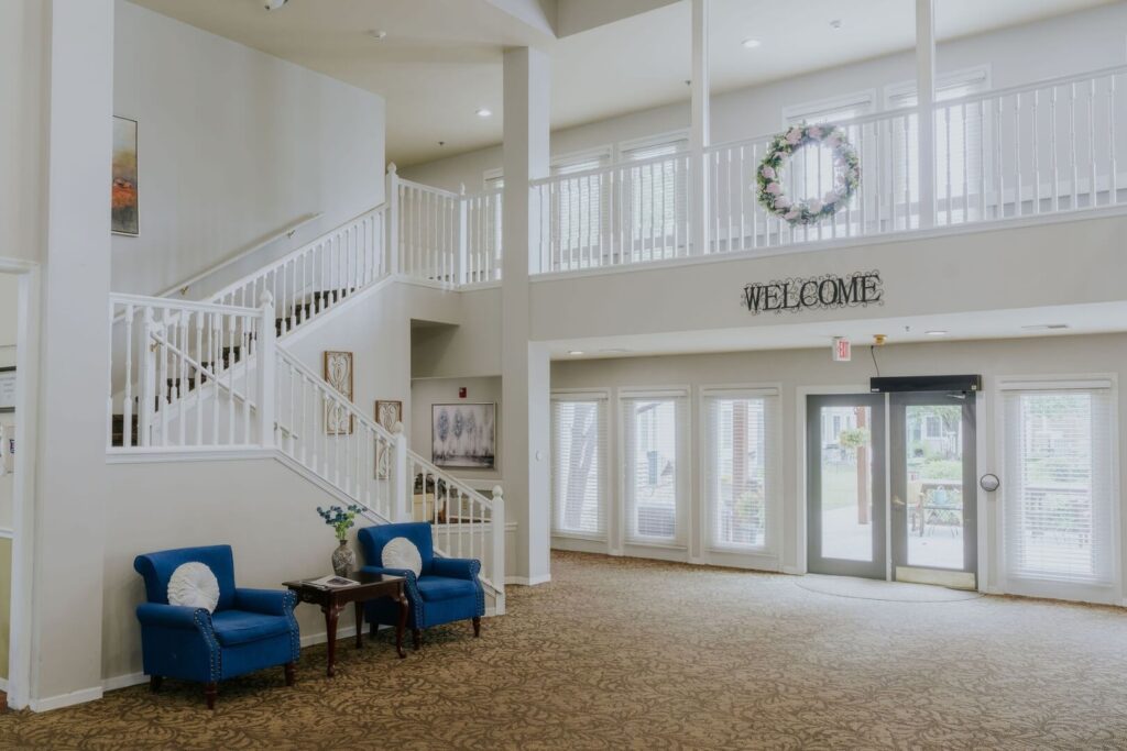 Open Welcoming Lobby With Grand Staircase And Entry Doors At Assisted Living Facility