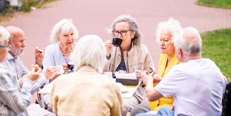 Group of Elderly Friends Enjoying Coffee Together Outdoors at Assisted Living Facility